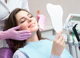 Patient smiling into mirror with dentist framing her cheeks with purple gloved hands