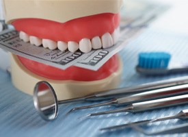 Artificial jaw mockup with money and dental instrument on table.