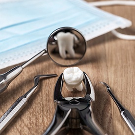 Extracted tooth on wooden surface with dental instruments reflected in mirror
