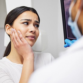 Woman holding hand to jaw in pain looking at screen dentist is pointing to