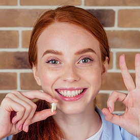 Woman making OK sign with one hand and holding extracted tooth in the other