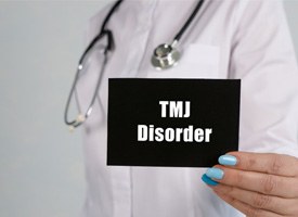 Female dentist holding a card that says “TMJ Disorder”