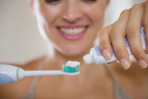 person putting toothpaste on an electric toothbrush 