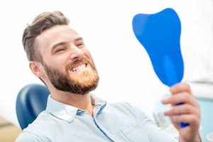 Man with holistic dental implants smiling in mirror